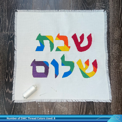 Cross-stitched fabric with colorful Hebrew text on a wooden surface