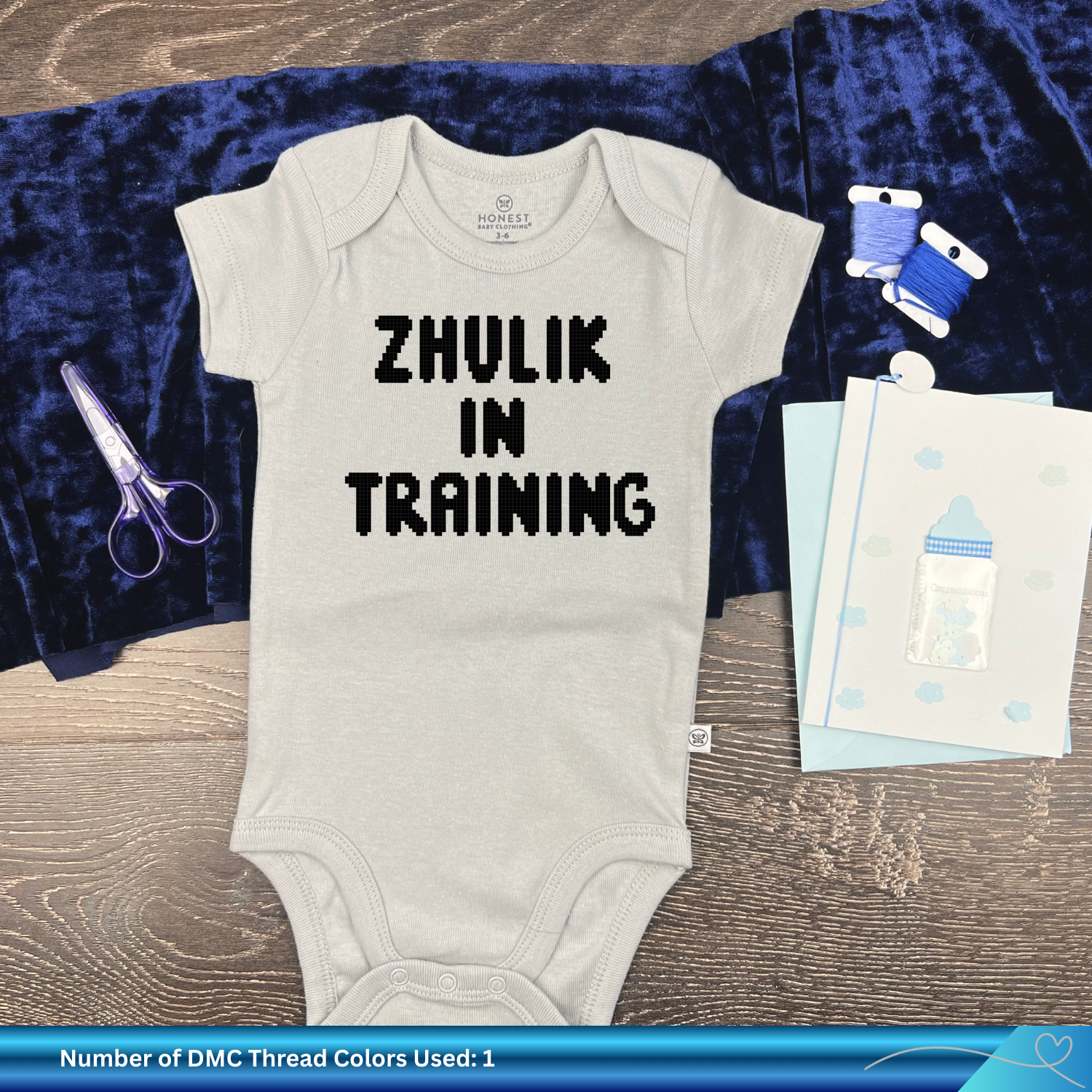Baby onesie with 'ZHULIK IN TRAINING' text on a blue fabric background