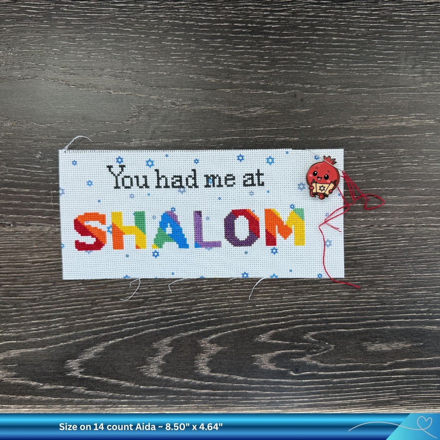 Cross-stitched project with 'You had me at SHALOM' and a needle minder on a wooden surface