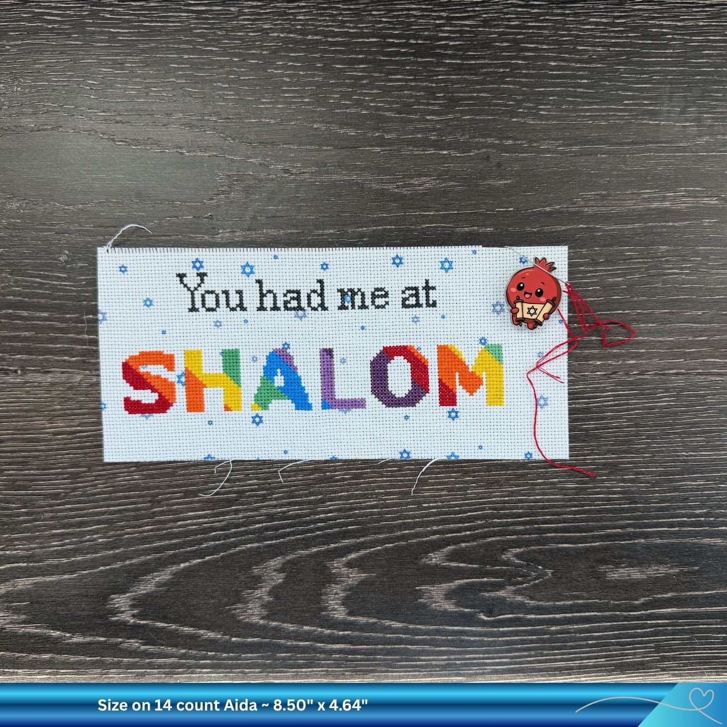 Cross-stitched project with 'You had me at SHALOM' and a needle minder on a wooden surface