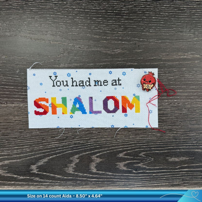 Cross-stitched project with 'You had me at SHALOM' and a needle minder on a wooden surface