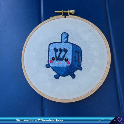 Embroidery of a cute hand-stitched dreidel with a wooden hoop on a blue background