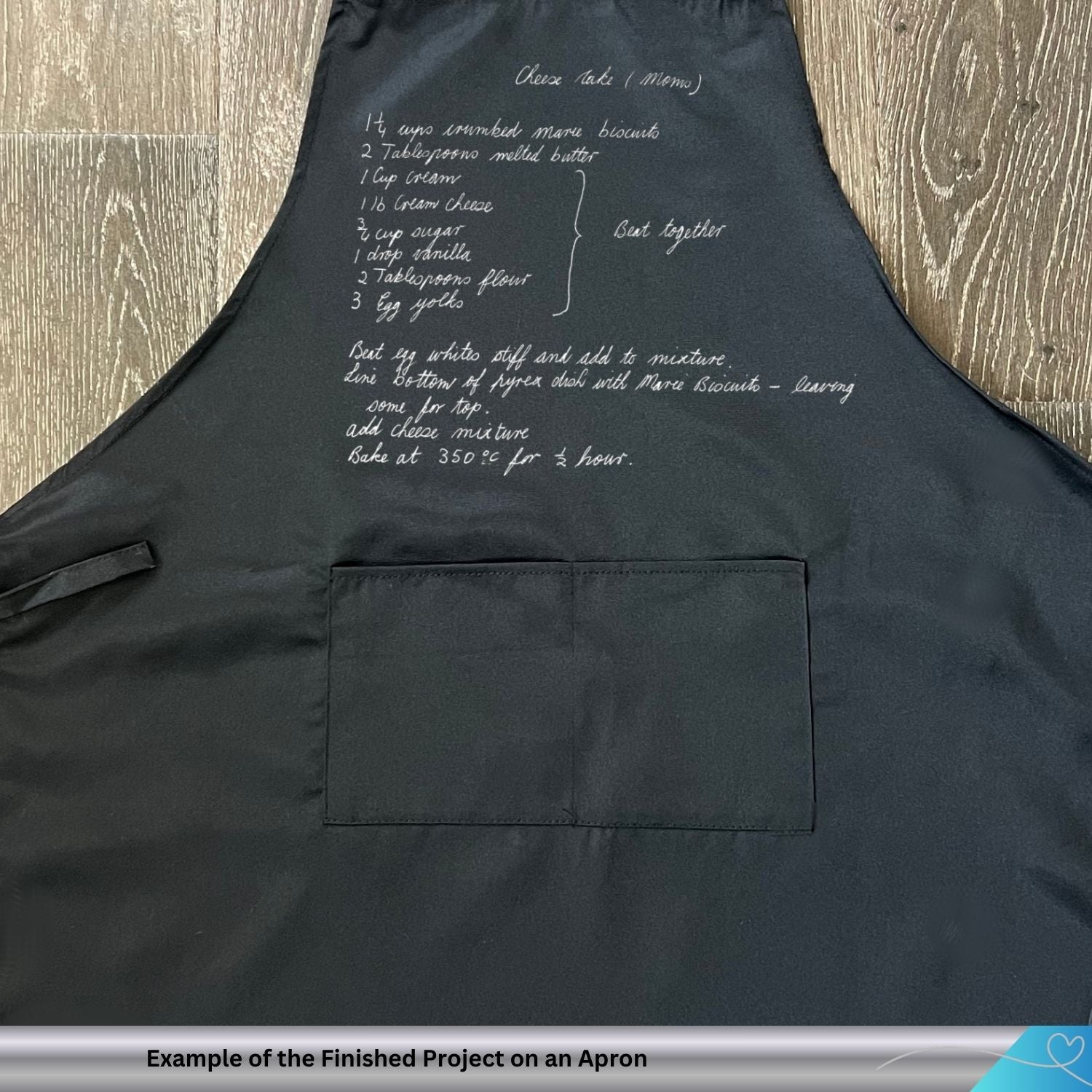 Black apron with white text hand embroidered on a wooden surface