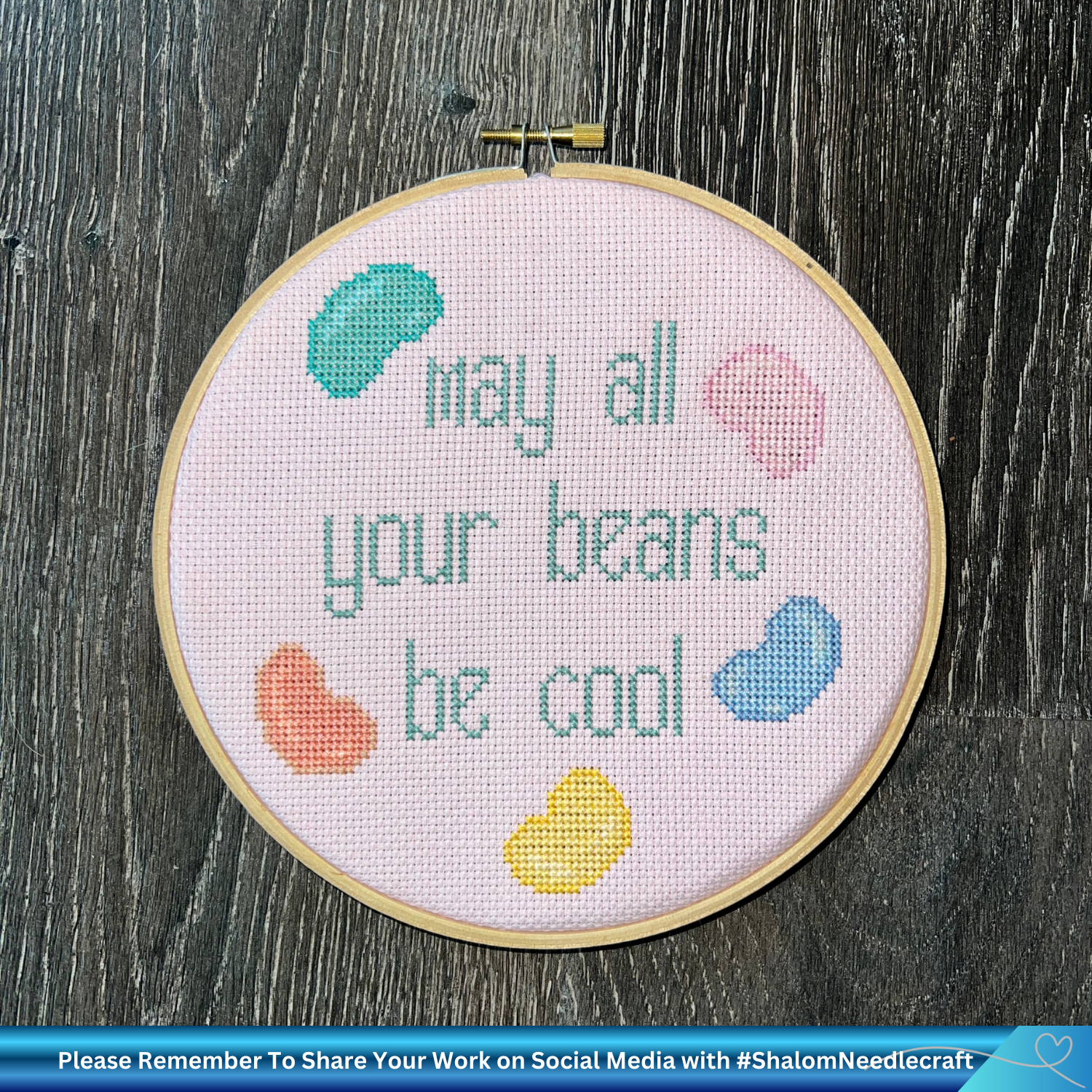 Embroidery hoop with cross-stitched text and colorful beans on a wooden surface