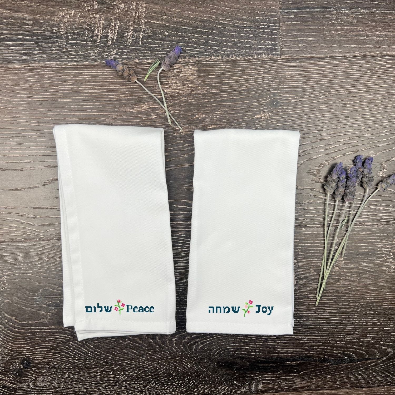 Two white napkins with embroidered Hebrew text on a wooden surface with lavender.