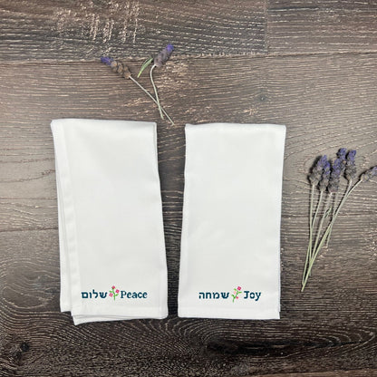 Two white napkins with embroidered Hebrew text on a wooden surface with lavender.