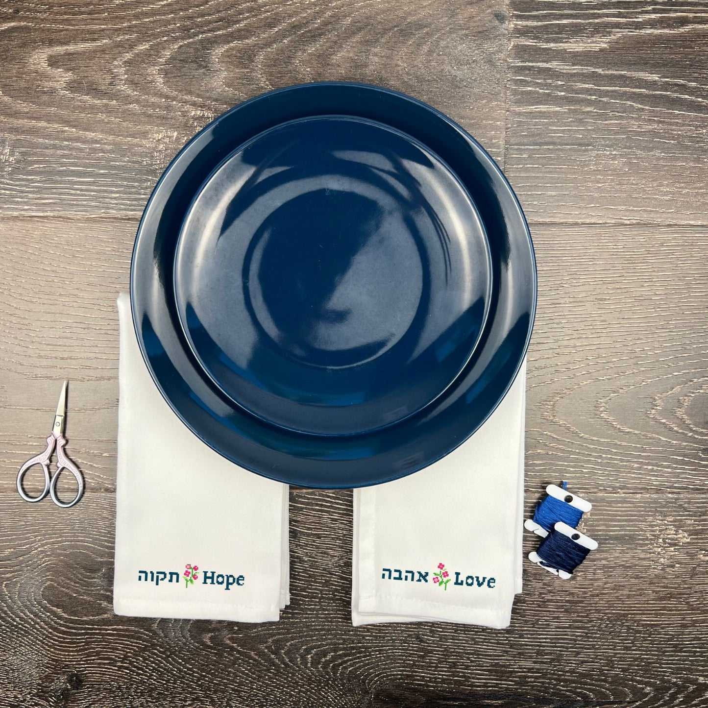 Blue ceramic plate on a wooden surface with 'Hope' and 'Love' hand embroidered towels and scissors.