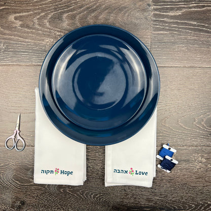 Blue ceramic plate on a wooden surface with 'Hope' and 'Love' hand embroidered towels and scissors.