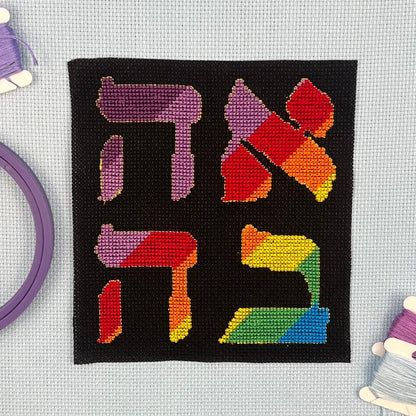 Cross-stitched word Ahava in Hebrew with rainbow letters on a black Aida background