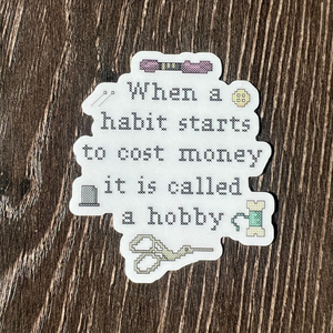 Sticker with cross-stitch-style text with a funny saying on a wooden surface