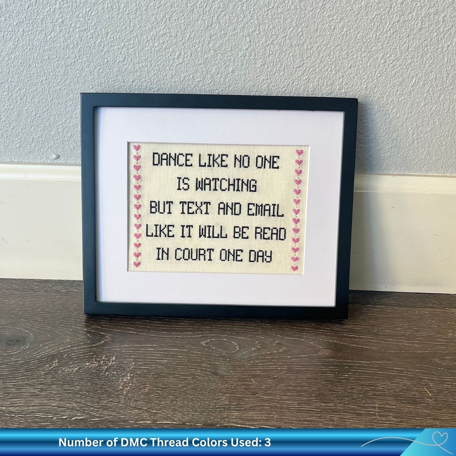 Cross stitch pattern with the phrase "dance like no one is watching but text and email like it will be read in court one day" framed against the wall.