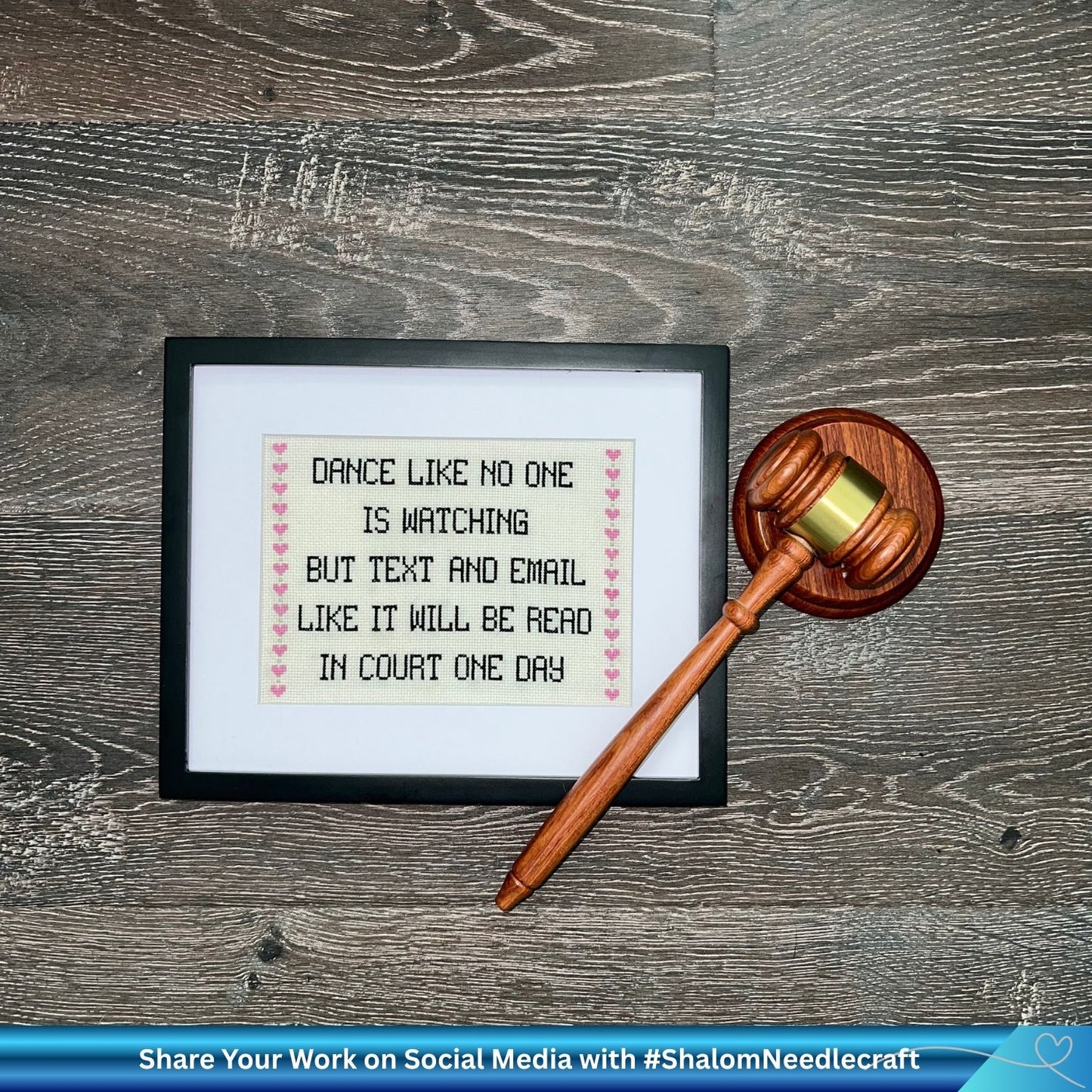 Framed cross-stitched daily quote with a gavel on a wooden surface