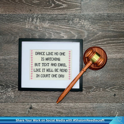 Framed cross-stitched daily quote with a gavel on a wooden surface