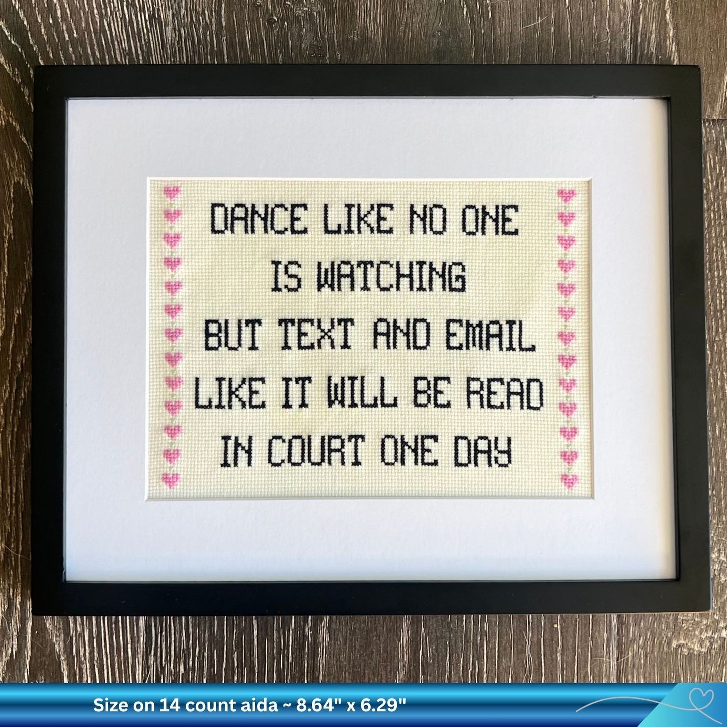 Framed humorous legal cross-stitched text on a wooden surface