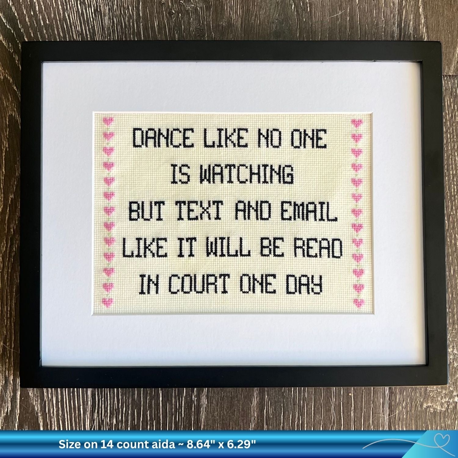 Framed humorous legal cross-stitched text on a wooden surface