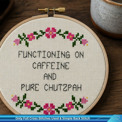 Finished cross-stitch pattern with text 'Functioning on caffeine and pure chutzpah' on a wooden background