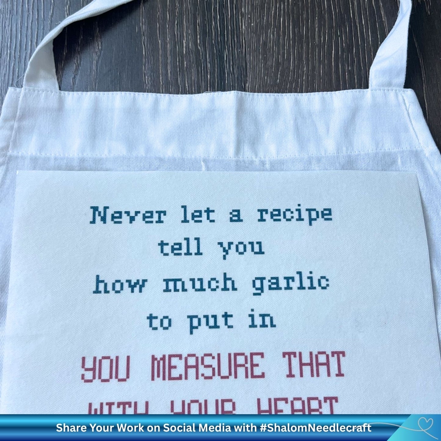 Cross stitch phrase printed onto stick and stitch fabric about to be adhered to the front of a white apron for stitching