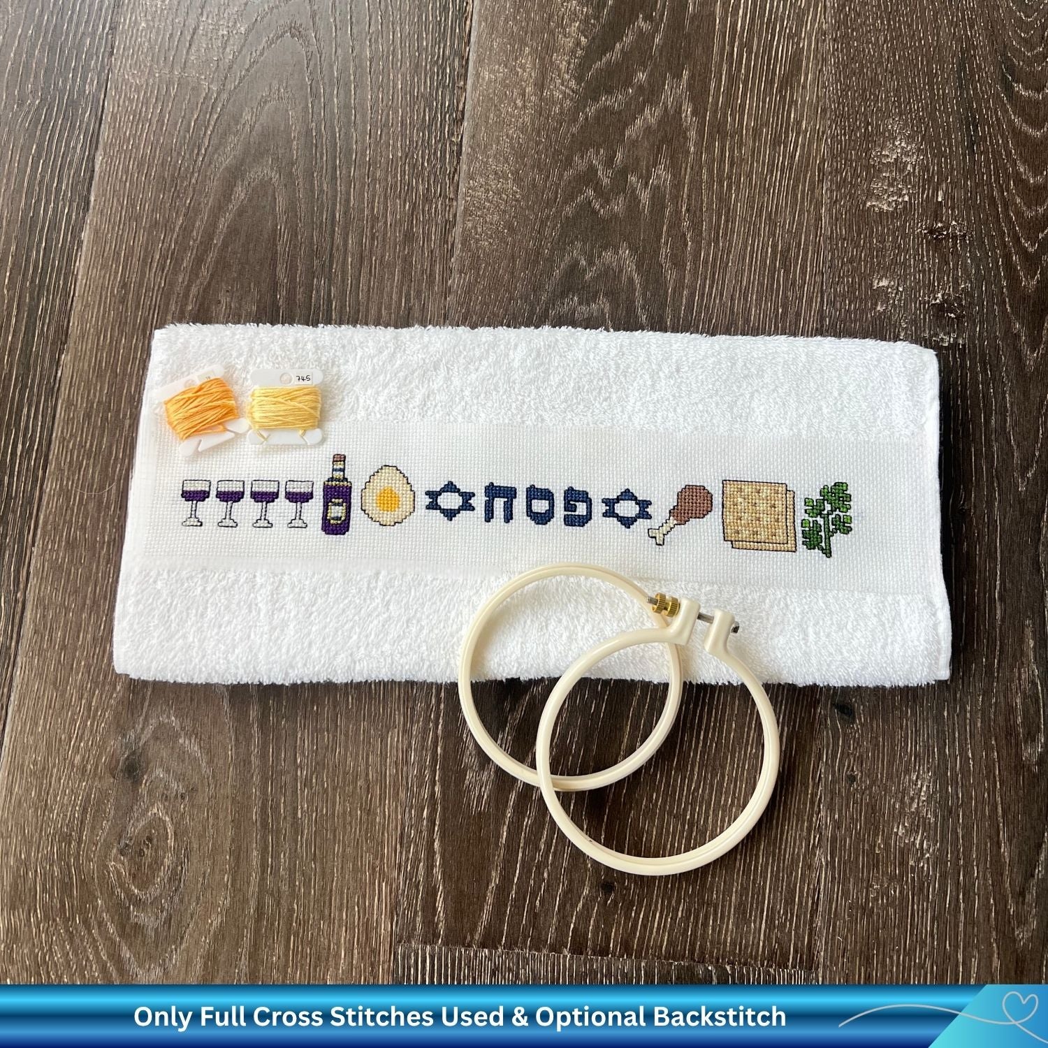 Hand cross-stitched Passover towel  with embroidery thread and white embroidery hoop on a wooden background
