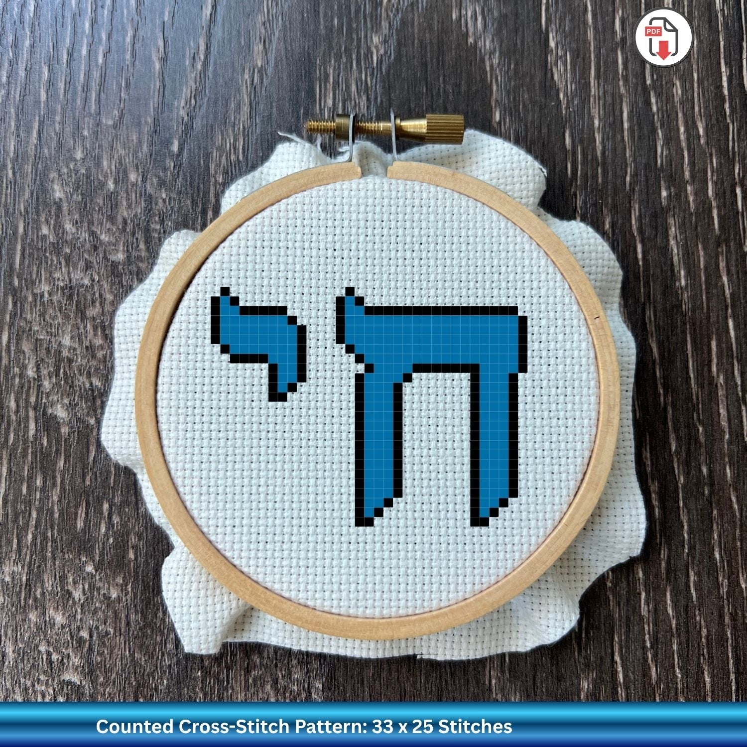 Embroidery hoop with blue Hebrew lettering on white cross stitch fabric against a wooden background