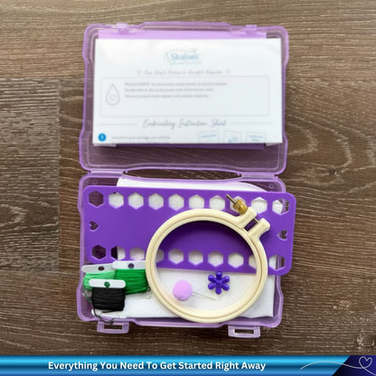Embroidery kit with hoop, thread, and tools in a purple case on a wooden surface.