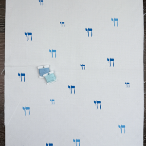 White cross-stitch fabric with blue Hebrew Chai in Hebrew characters on a wooden surface