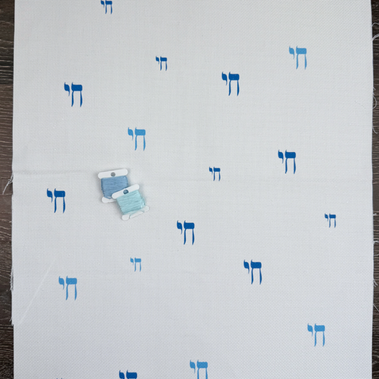 White cross-stitch fabric with blue Hebrew Chai in Hebrew characters on a wooden surface