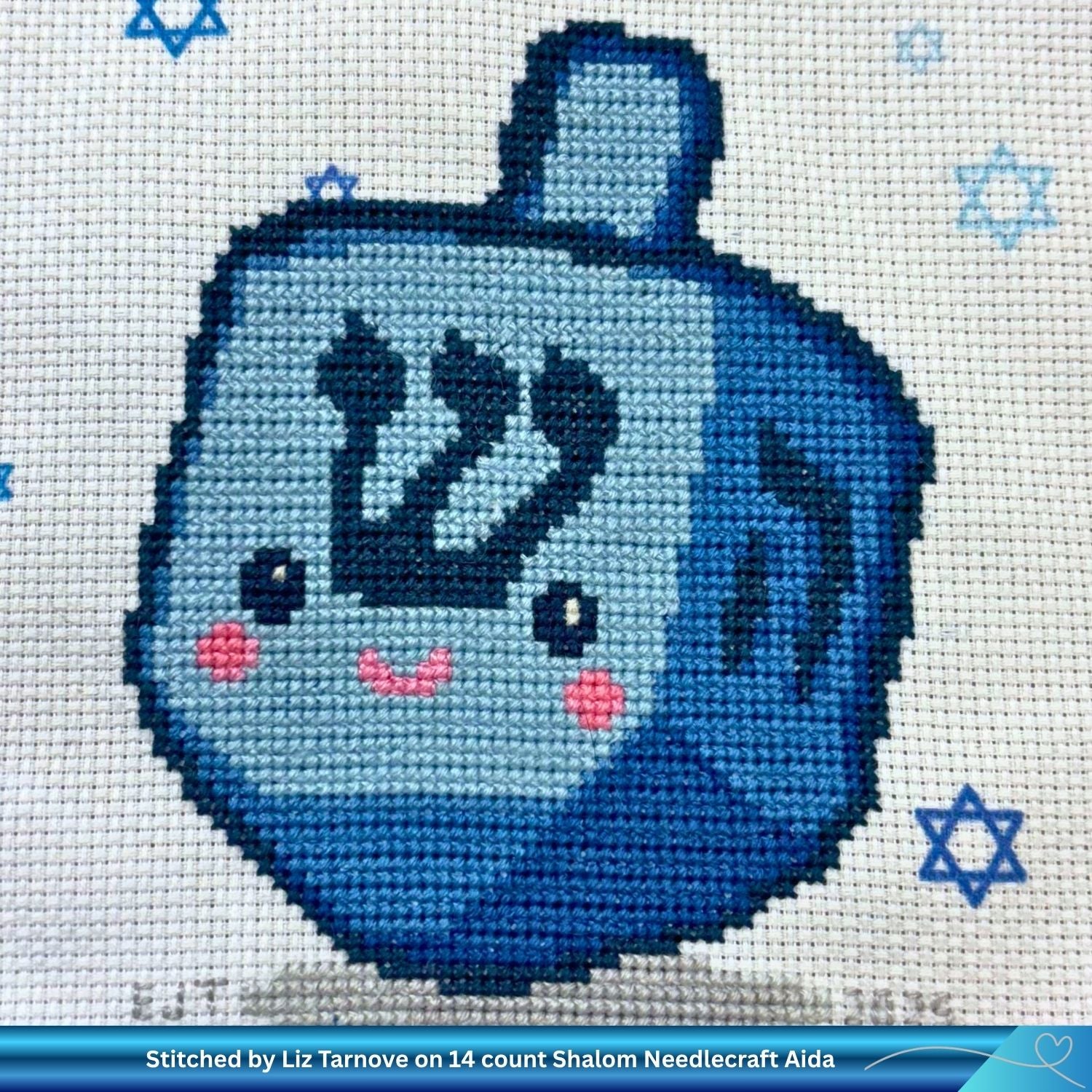 Cross-stitched design of Shlomo the Hanukkah dreidel on star of david Aida