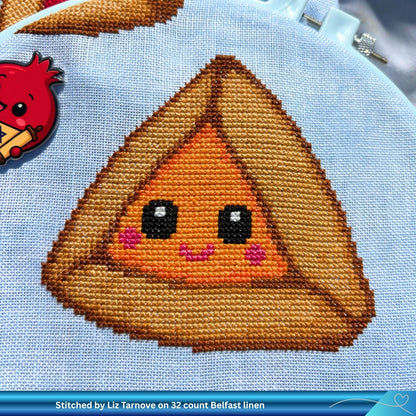 Cross-stitched design of a cute apricot Hamantaschen character on linen fabric.