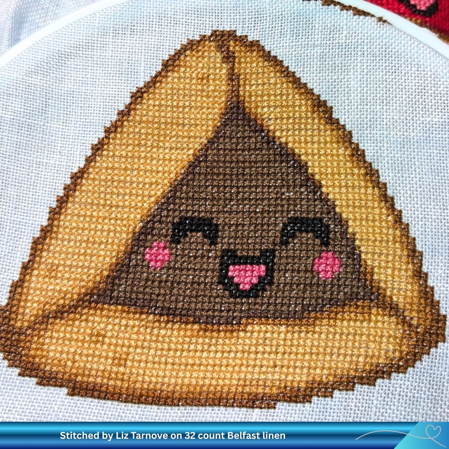 Cross-stitched design of a smiling chocolate Hamantaschen character on linen fabric.