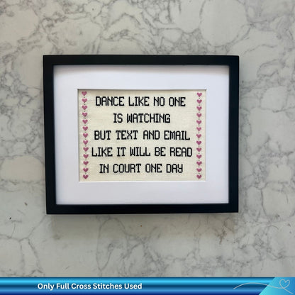 Framed cross-stitched quote against a white marble background, The quote says: "Dance like no one is watching but text and email like it will be read in court one day" 