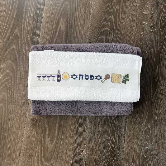 Folded towel with embroidered Passover symbols on a wooden surface
