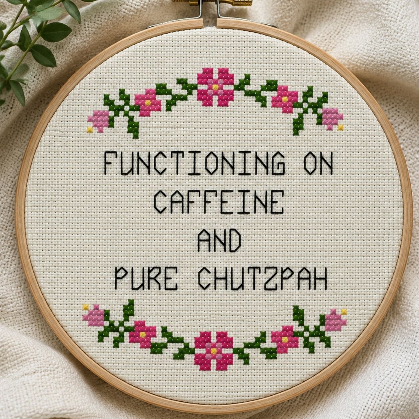 Cross-stitched hoop with text 'Functioning on caffeine and pure chutzpah' on a fabric background