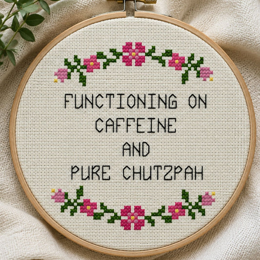 Cross-stitched hoop with text 'Functioning on caffeine and pure chutzpah' on a fabric background
