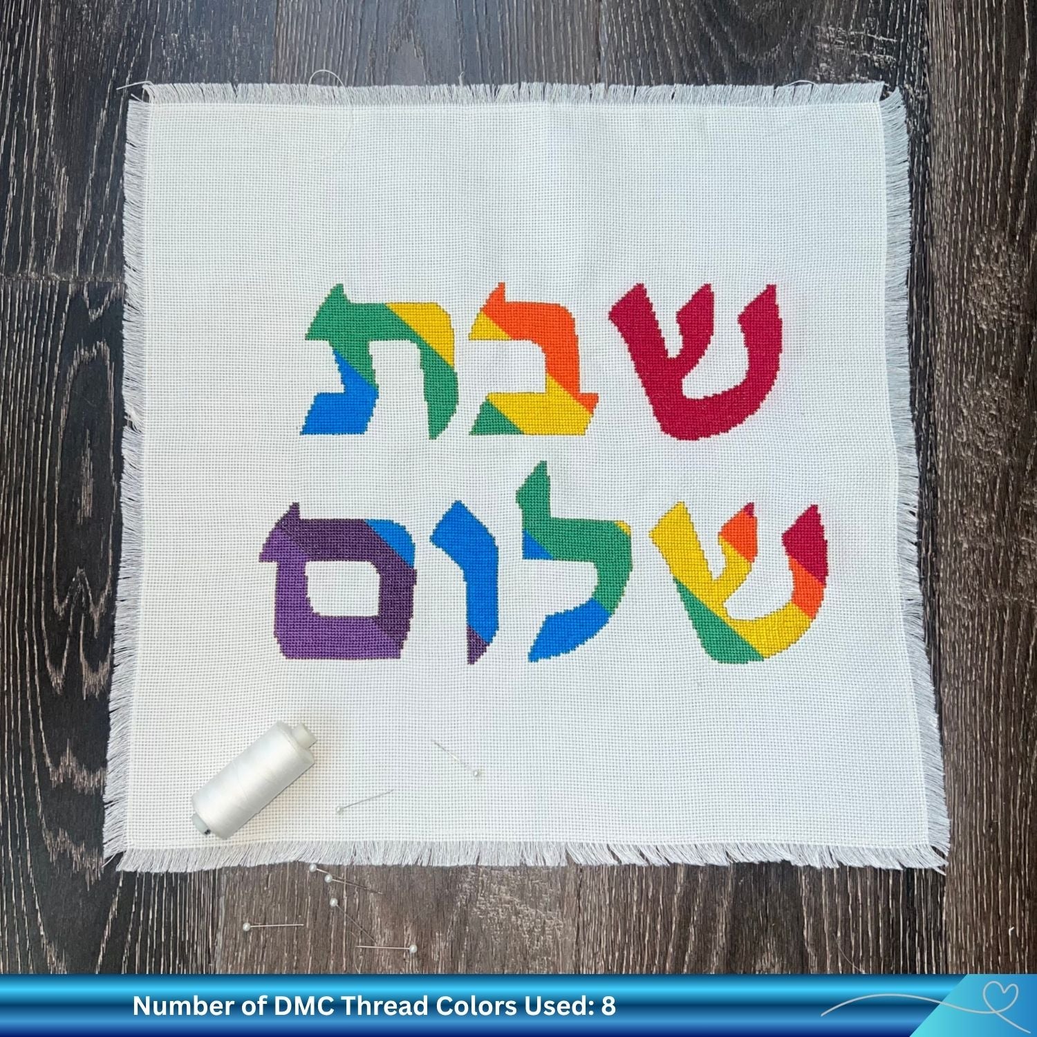 Rainbow colored Shabbat Shalom cross stitch design on challah cover against a wooden background