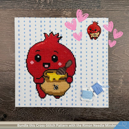 A cross-stitch pattern preview showing a cute red pomegranate character holding a yellow honey jar, stitched on white Aida cloth with light blue Hamsa hands. Pink hearts encircle a matching RImon pomegranate needle minder. The text banner at the bottom reads 'Bundle this Cross-Stitch Pattern with the Matching Needle Minder'.