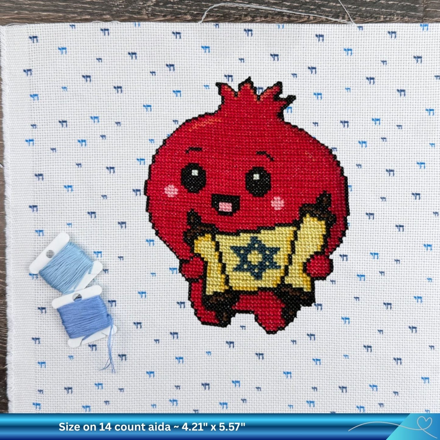 Cross-stitch pattern of a red Pomegranate holding a Torah scroll with blue thread on a white Aida fabric background.