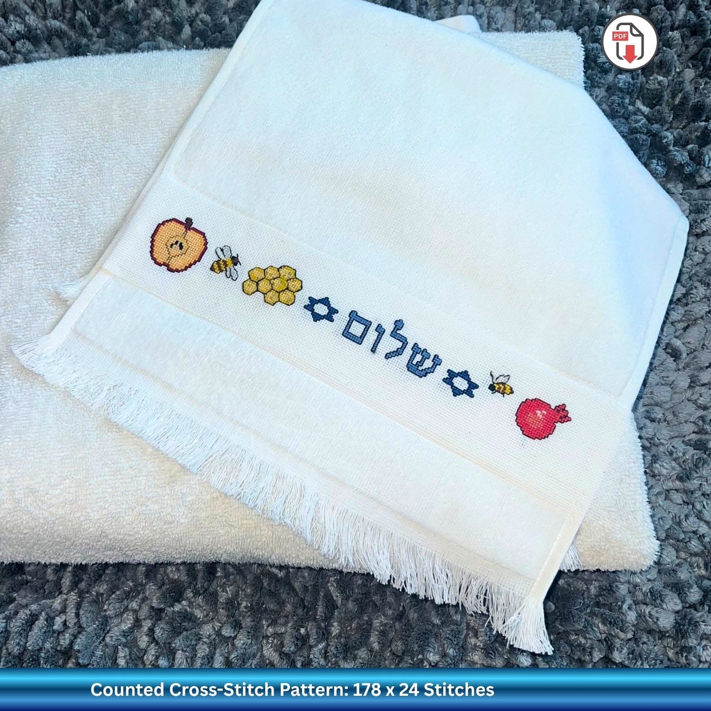 Folded white towel with embroidered Rosh Hashanah Jewish New Years designs on a textured surface