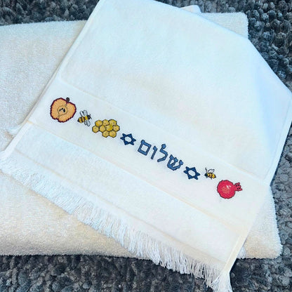 Folded white towel with embroidered Rosh Hashanah Jewish New Year's designs on a textured surface