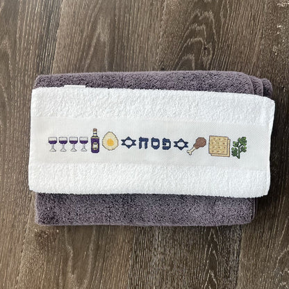 Cross-stitched Pesach design on a towel neatly folded against a wooden surface.