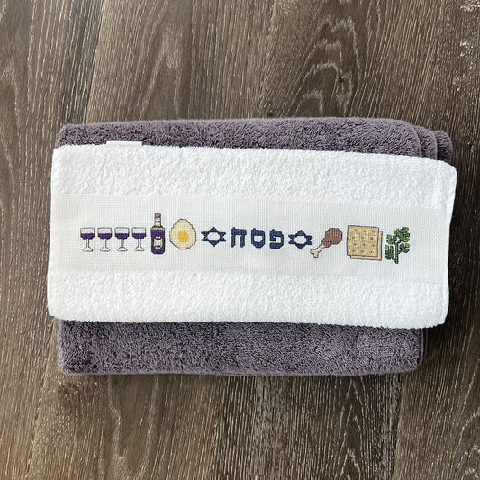 Cross-stitched Pesach design on a towel neatly folded against a wooden surface.