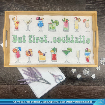 Cross-stitched pattern with cocktail designs and 'But first... cocktails' text on a wooden tray. There are also embroidery items and some lavender around the tray for summer.